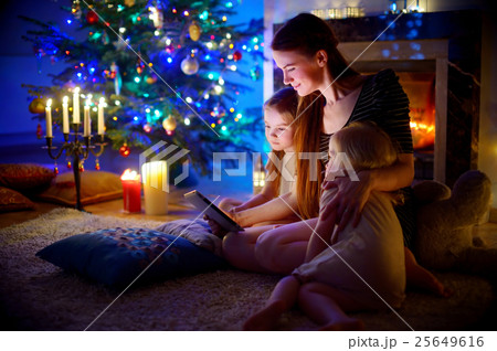 Mother and daughters using a tablet by a fireplace on Christmas 25649616