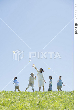 草原で紙飛行機を飛ばす小学生と先生 25655236