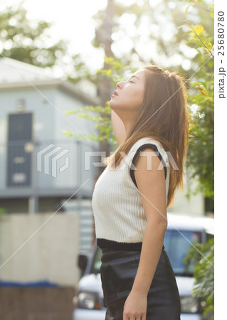 ポートレート 女性 立つ 見上げる 目を閉じる 夏 逆光 太陽 緑 ノースリーブ 屋外 横顔の写真素材