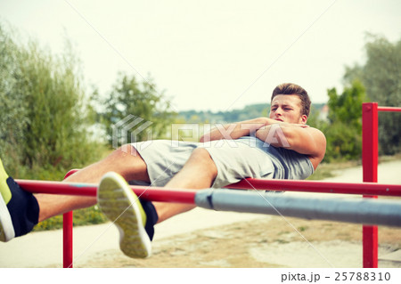 young man doing sit up on parallel bars outdoors 25788310