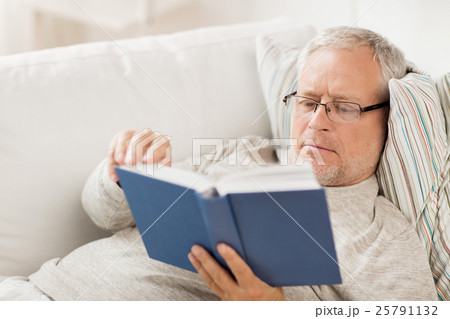 senior man lying on sofa and reading book at home 25791132