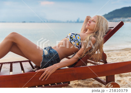 slim blonde woman gets suntan on sunbed near sea 25810379