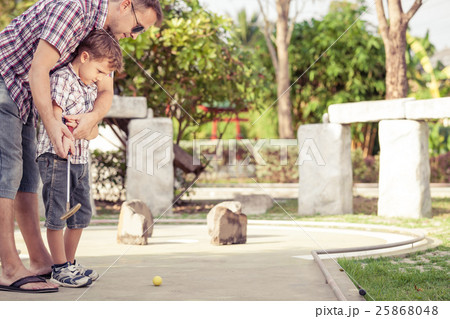 Cheerful young man teaching his son to play mini golf at the day 25868048