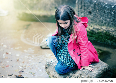 pretty little girl playing on a rock at the water's edge 26038250