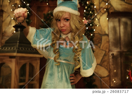 Snow Maiden holds lantern on doorstep of house decorated in Christmas style 26083717