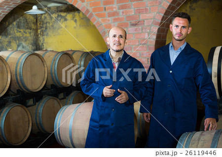 two cheerful men in uniforms standing in cellar with wine woods 26119446