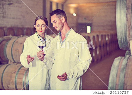 Portrait of young man and woman holding glass of wine in winery 26119737