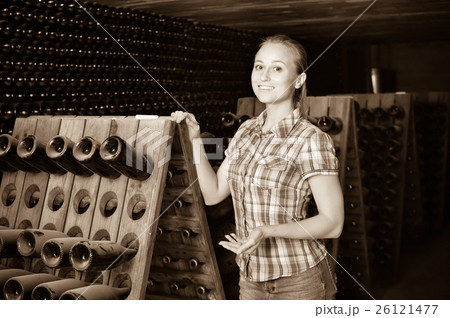 Woman winery employee standing in aging section with bottles 26121477