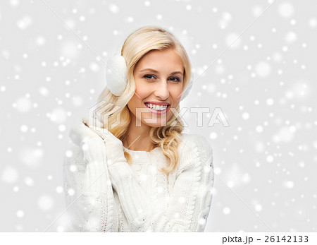 smiling young woman in winter earmuffs and sweater 26142133