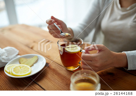 close up of woman adding honey to tea with lemon 26144168