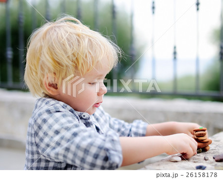 Cute blonde little boy playing with little stones outdoors Cute blonde little boy playing with little stones outdoors 26158178