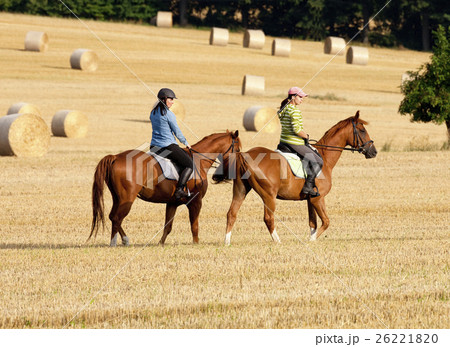 Two Women Horseback Riding in a Field with Bales of Hay 26221820
