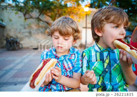 Two little kid boys eating hot dogs outdoors 26221835