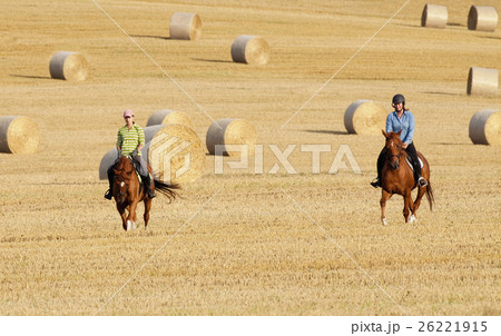 Two Women Horseback Riding in a Field with Bales of Hay 26221915