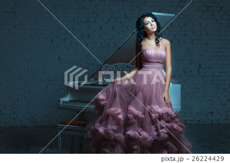 Beautiful woman posing next to a white piano. 26224429