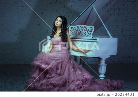 In a dark room girl sitting at the piano. 26224431