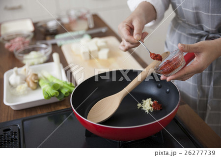 ニンニクと豆板醤をフライパンに入れる女性 26277739