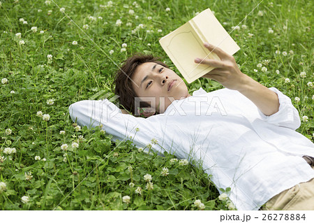 野原に寝転んで本を読む男性の写真素材