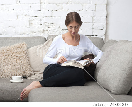 Girl sitting on couch with and reading a book 26300038