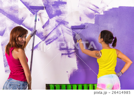 women paints white wall with purple paint roller 26414985