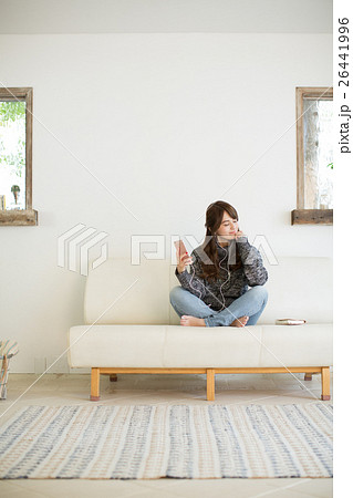リビングのソファーでくつろぎながら音楽を聴く若い女性の写真素材