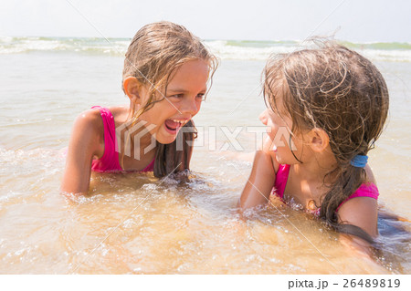 Two girls lying in the shallow water and have fun looking at each other 26489819