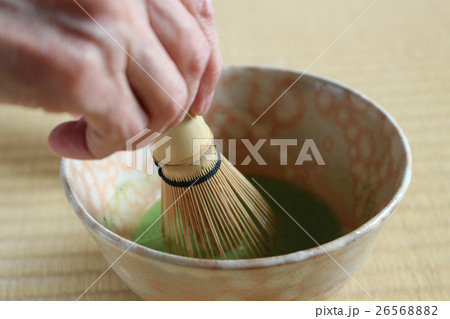 畳の上でピンク色の萩茶碗で右手で茶筅を持ち抹茶を泡立てる 26568882
