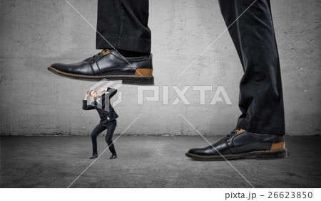 Tiny frightened businessman under feet of huge man 26623850