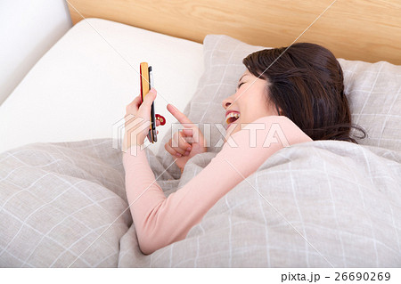 ベッド 写真はイメージです。 ベッドでスマホをいじる女性 寝ながらスマホの写真素材 [26690269] - PIXTA