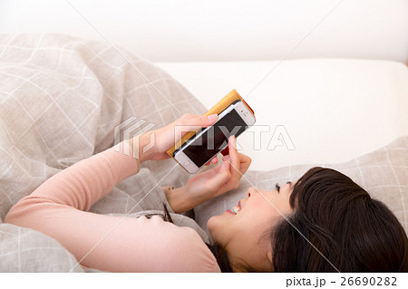 ベッドでスマホをいじる女性 寝ながらスマホの写真素材