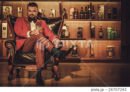 Extravagant stylish man with whisky glass sitting 26707265