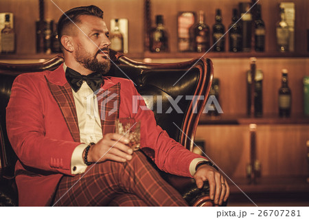 Extravagant stylish man with whisky glass sitting 26707281
