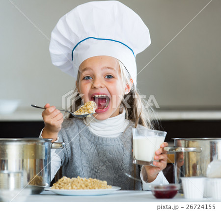 Cheerful girl in cook cap eating porridge indoors 26724155