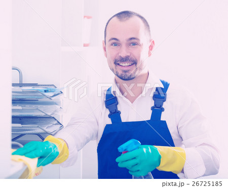 Young man in apron cleaning shelves 26725185