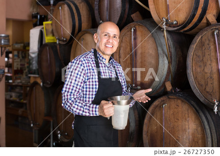 Smiling mature man seller pouring wine from wood Smiling mature man seller pouring wine from wood 26727350