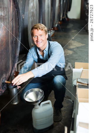 man pouring wine from wood in cellar . man pouring wine from wood in cellar . 26727623