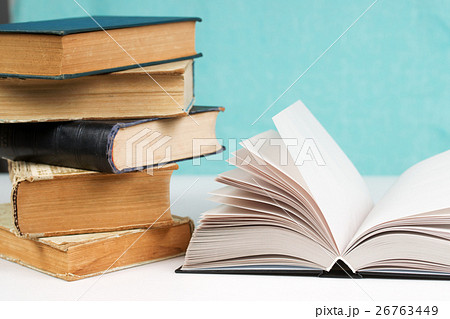 Open book, stack of hardback books on table. 26763449