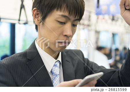 吊革につかまりながら電車内でスマホを操作する男性　ビジネスマン　通勤　朝 26815599