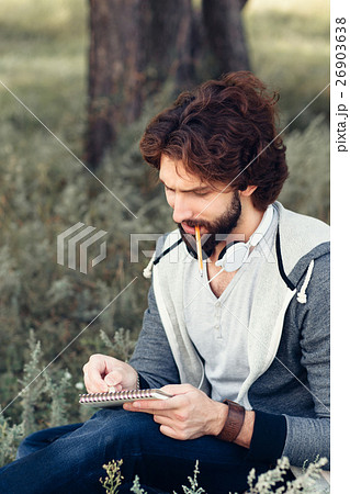 Close-up of man with notebook biting pencil Close-up of man with notebook biting pencil 26903638