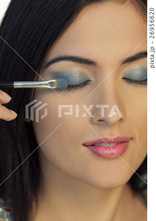 Head shot of young woman putting on blue eyeshadow Head shot of young woman putting on blue eyeshadow 26956620