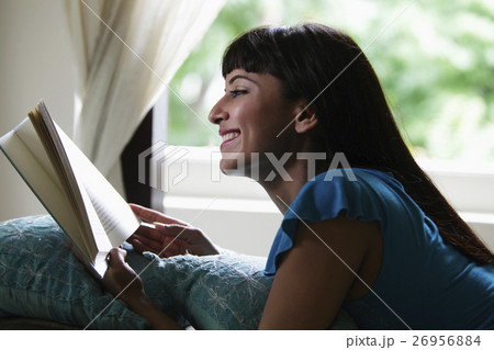 Young woman laying on stomach reading a book and smiling Young woman laying on stomach reading a book and smiling 26956884