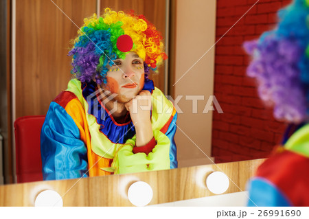 Circus clown looks in a mirror in makeup room. Circus clown looks in a mirror in makeup room. 26991690