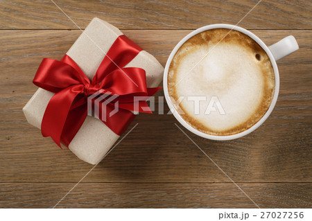cup of cappuccino and gift on wooden oak table top view 27027256