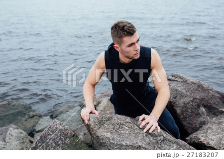 Strong man acts yoga on the rocks beach in the 27183207