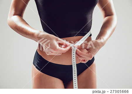 Athletic slim woman measuring her waist by measure Athletic slim woman measuring her waist by measure 27305666