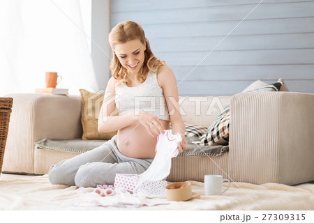 Pregnant woman discovering baby clothes Pregnant woman discovering baby clothes 27309315