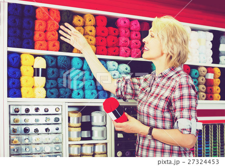 portrait of mature female customer standing next to shelf with knitting yarn in shop 27324453