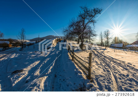fence on snowy rural field near village in winter 27392618