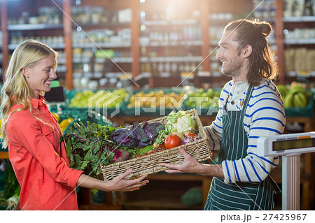 Male staff giving a crate of fresh vegetables to woman in organic section 27425967