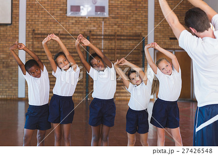 Teacher teaching exercise to school kids in basketball court Teacher teaching exercise to school kids in basketball court 27426548